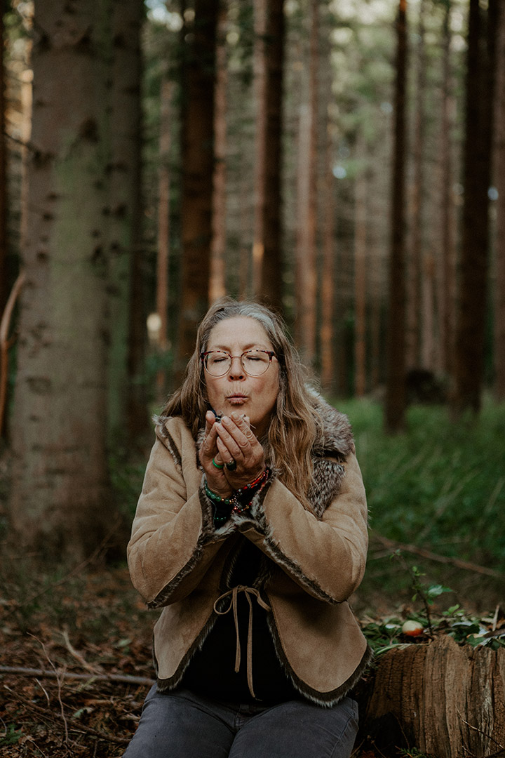 Naturterapeut, naturarbejder, shaman og healer Jeanne Jensen fra Naturlig Viis iklædt en skindjakke laver ild til kursus i årstidshjul i skoven